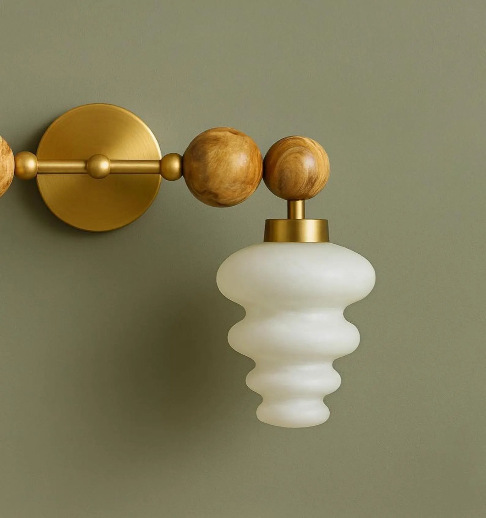 Wall-mounted light fixture with gold and wood accents on a green wall