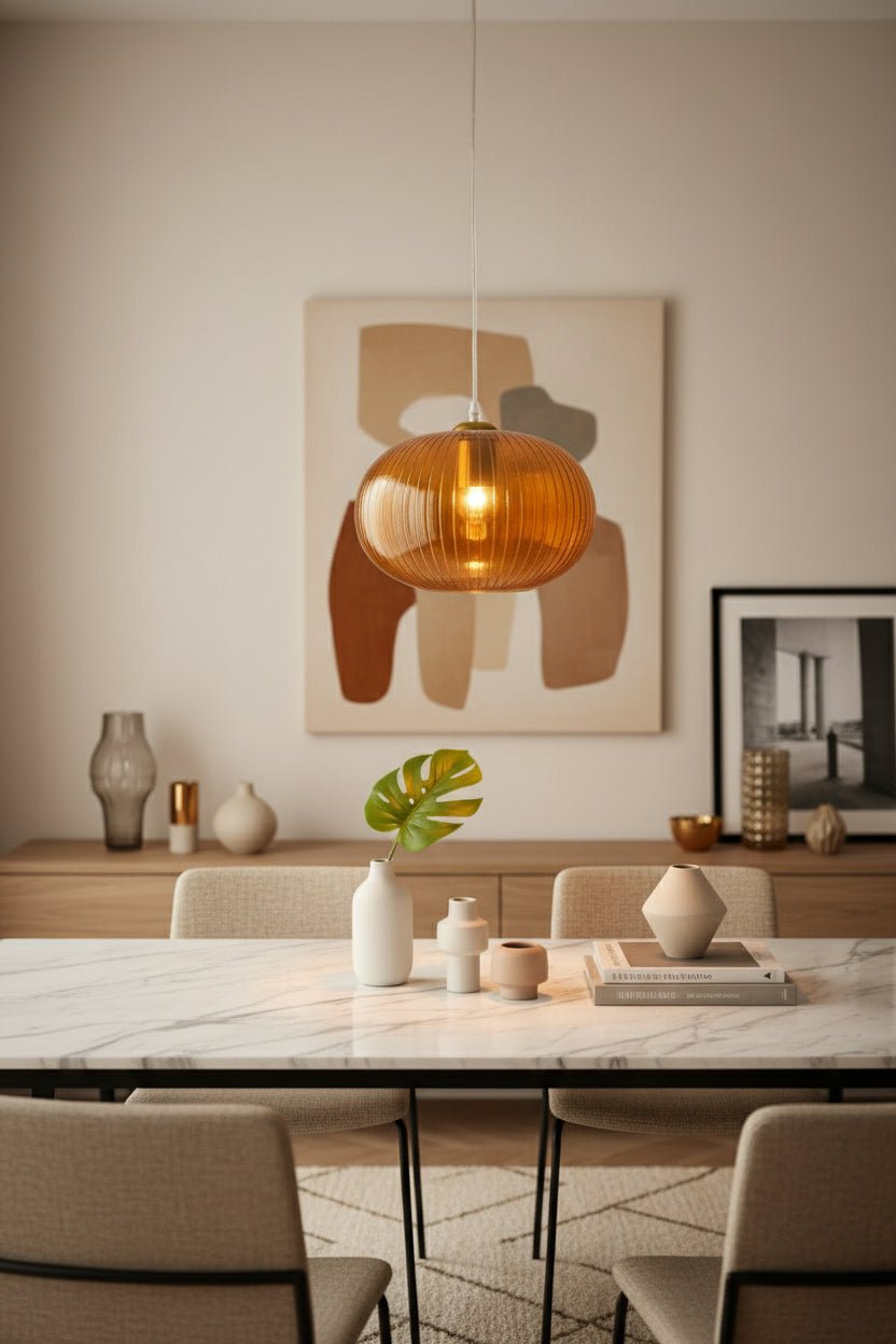 Orange pendant light hanging above a white vase with a plant on a neutral background