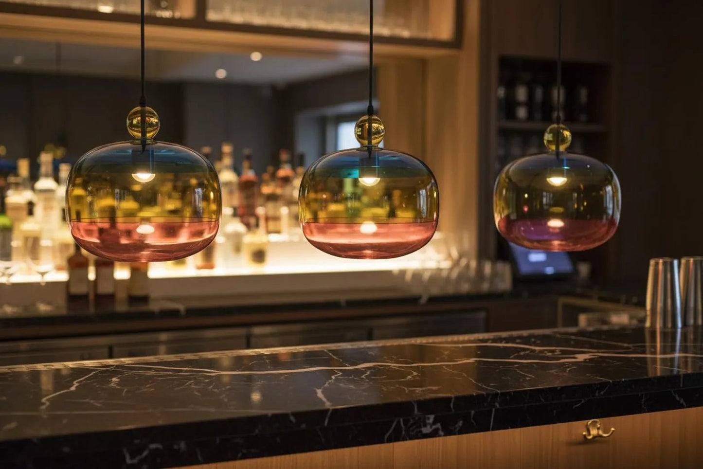 Three colorful pendant lights hanging above a bar counter with bottles in the background.