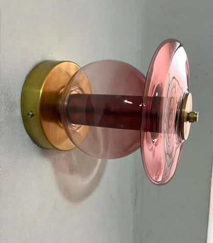 Pink glass door handle with gold metal finish on a white wall
