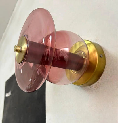 Pink glass door handle with gold metal finish on a white wall.