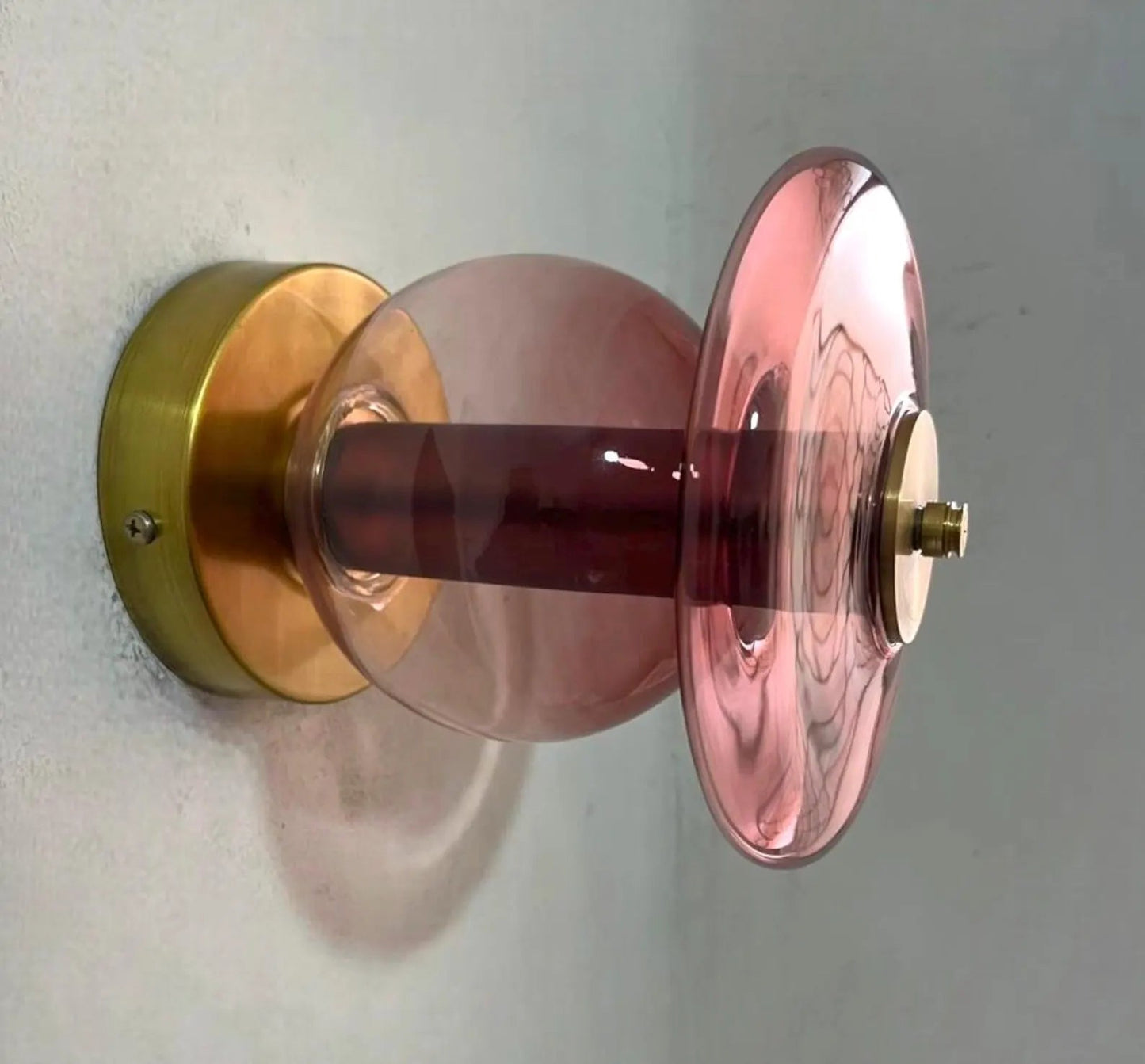 Decorative wall sconce with pink glass shade and gold metal base on a white wall.