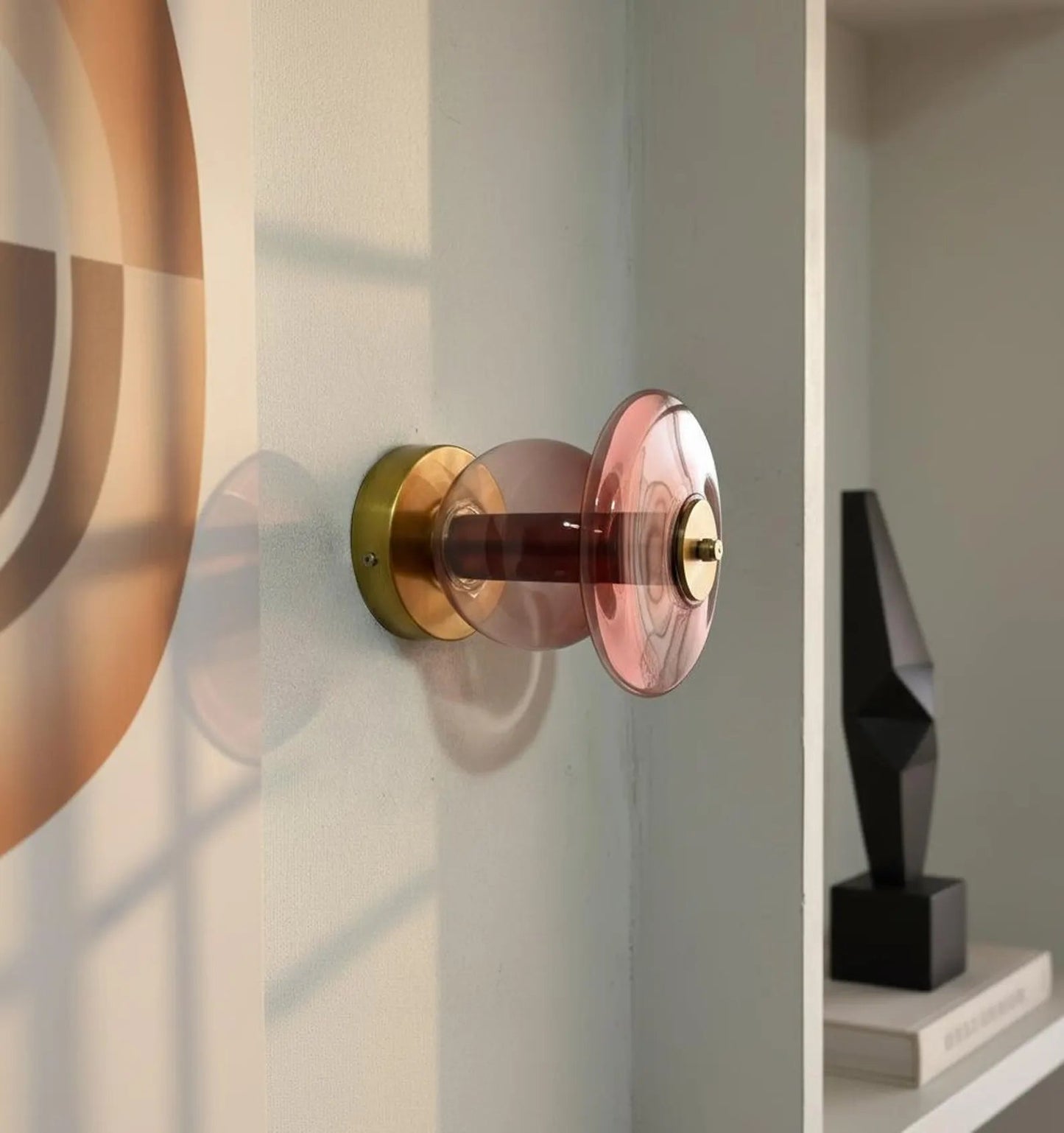 Decorative wall sconce with pink glass shade and gold metal fixture on a neutral wall.