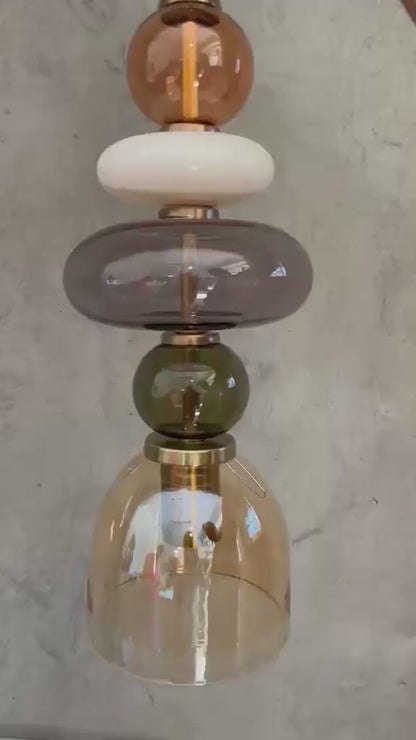 Handmade glass pendant light featuring amber, milky white, smoky grey and olive green glass elements, with brass accents and a clear champagne glass shade | Les Trois Pyramides