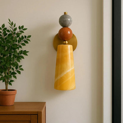 Decorative wall sconce with yellow and brown design on a beige wall next to a potted plant.