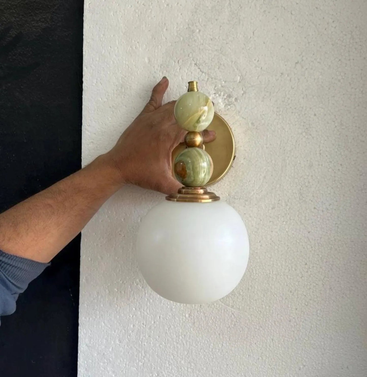 Hand adjusting a wall-mounted light fixture with marble accents on a plain wall.