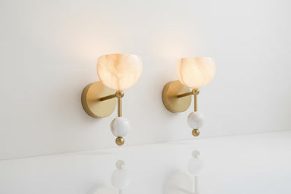 Two gold wall sconces with white spherical shades on a light gray wall.