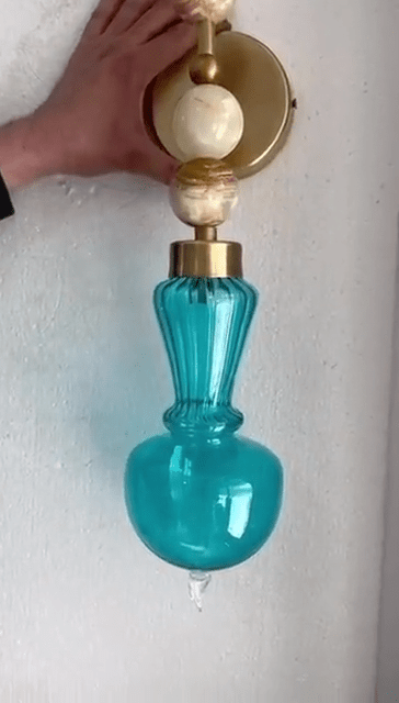 Turquoise glass wall sconce with gold accents on a white background
