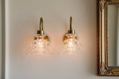 Hand-blown clear glass upside down bloom wall light with brass arm installed as a pair