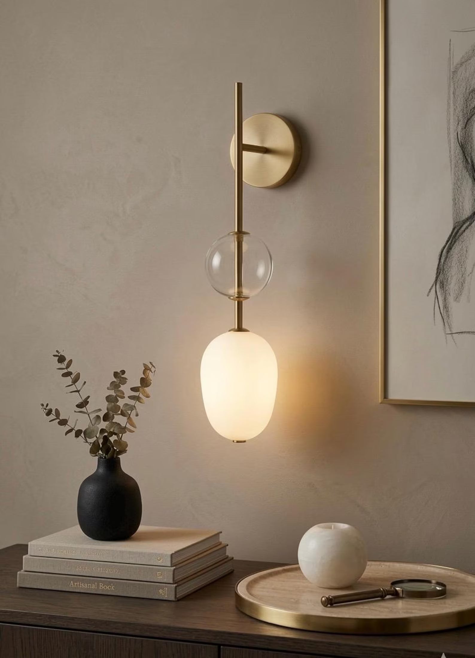 Modern wall sconce with a glass shade on a neutral wall with decor items below.