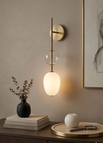 Modern wall sconce with a glass shade on a neutral wall with decor items below.