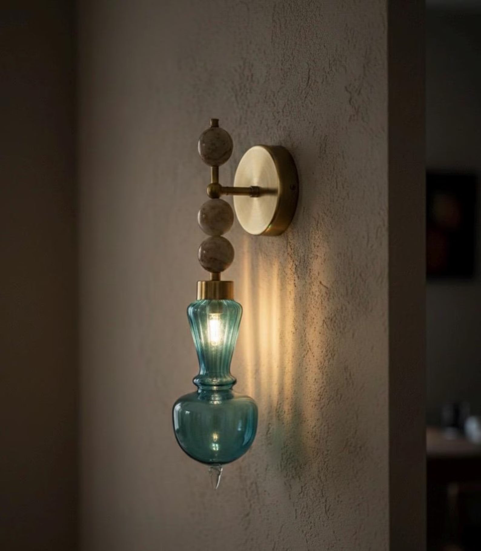 Wall-mounted light fixture with blue glass shade and gold accents on a textured wall.