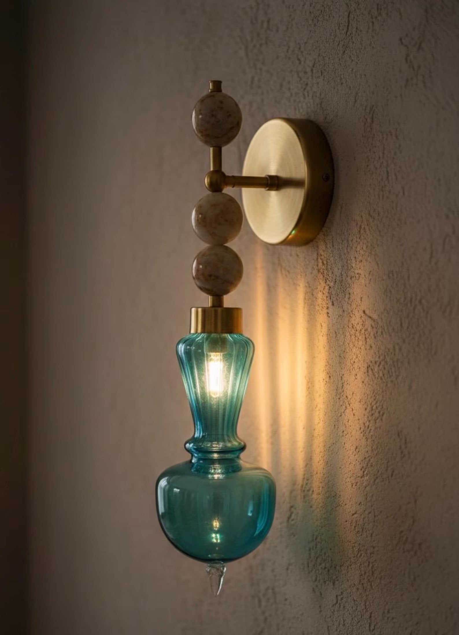 Wall-mounted light fixture with blue glass shade and gold accents on a textured wall.