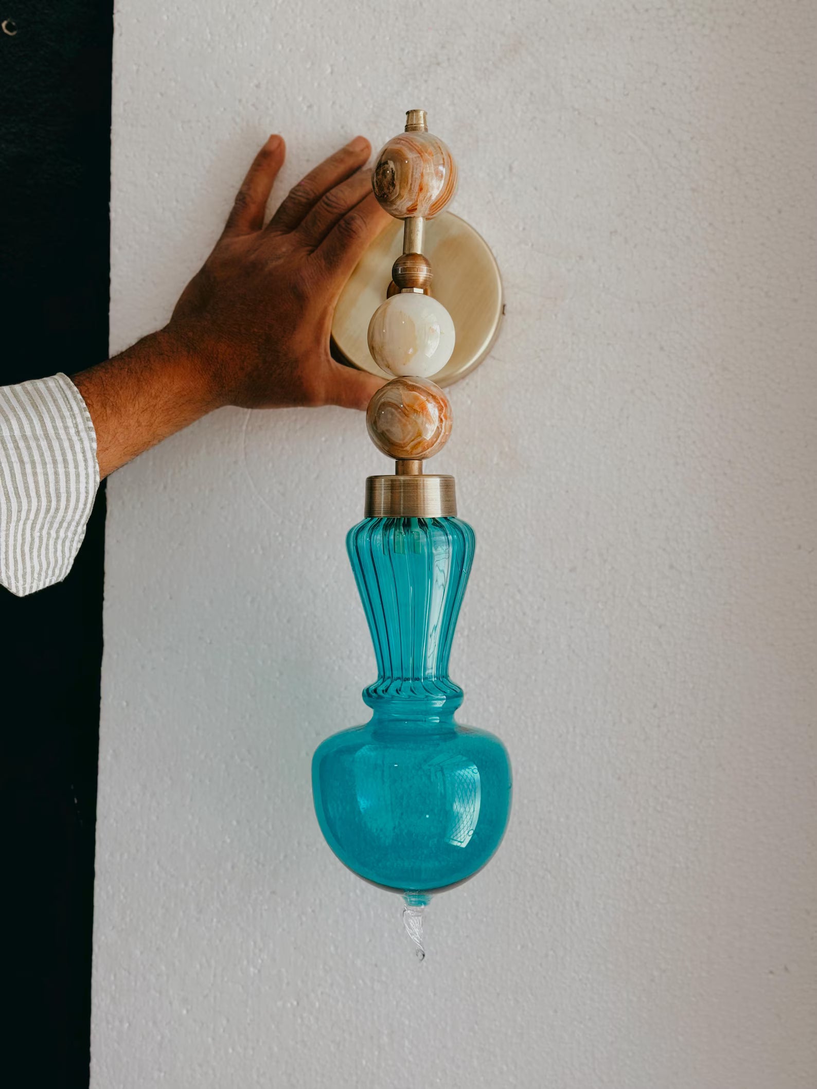 Person adjusting a decorative wall sconce with blue glass and marble accents.