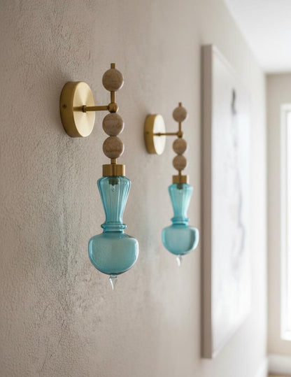 Two blue glass wall sconces with gold fixtures on a neutral wall.