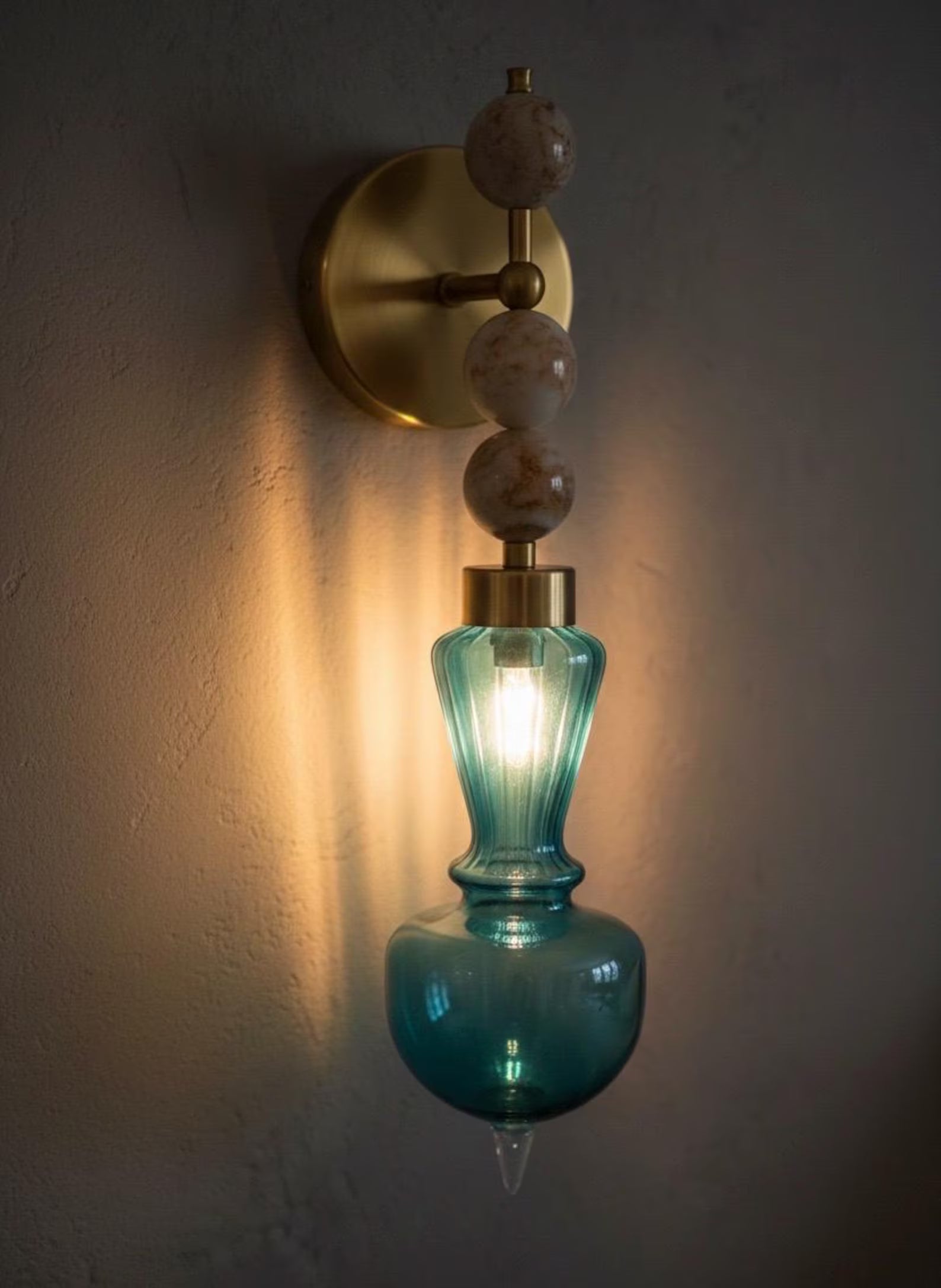 Wall-mounted light fixture with blue glass shade and gold fixture on a dark wall.