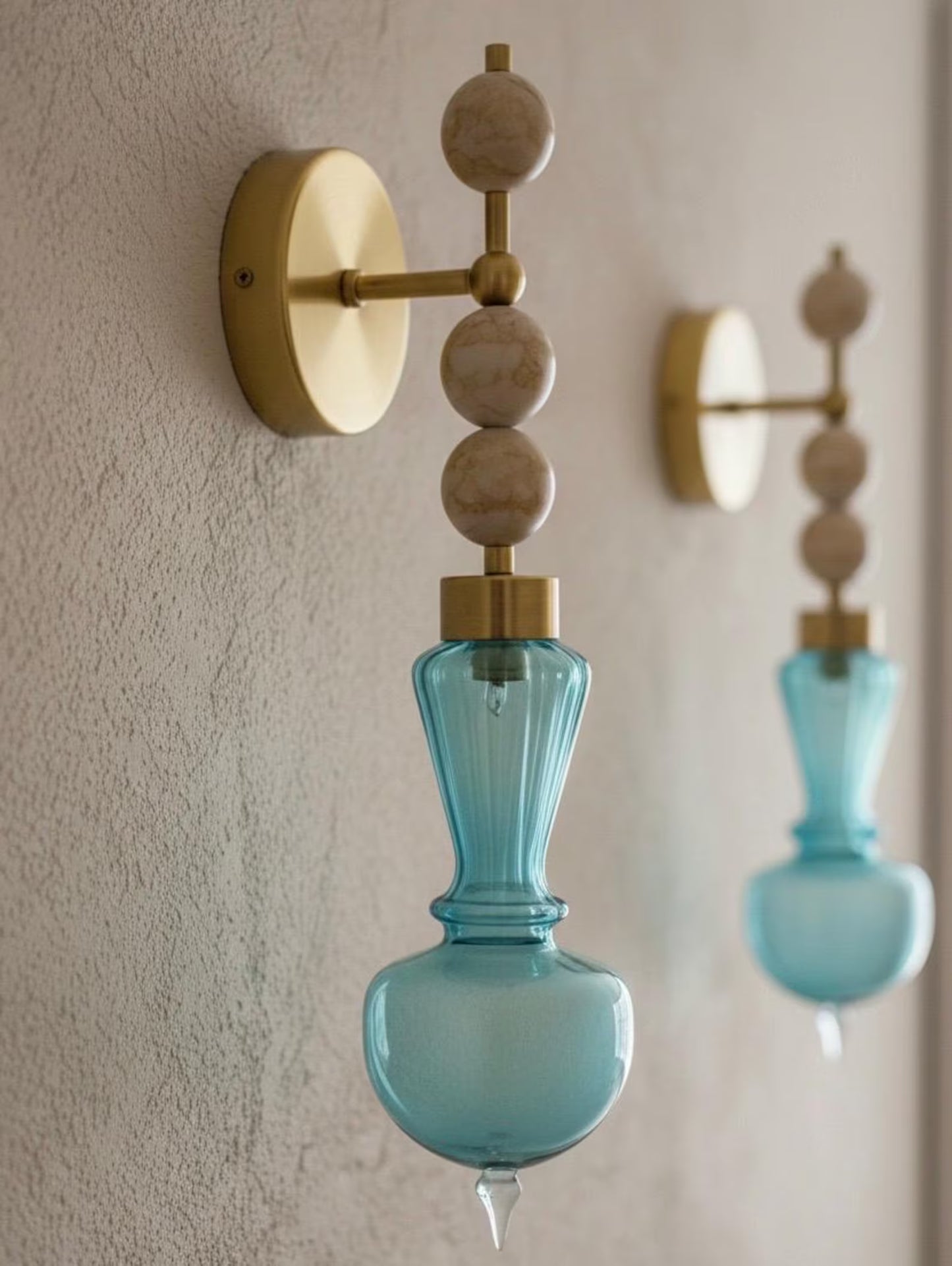 Wall-mounted light fixture with blue glass shade and gold accents on a beige wall.